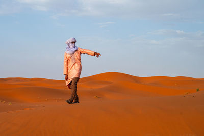 Rear view of man standing on sand at desert against sky