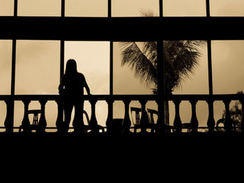 Silhouette woman standing by palm trees in city during sunset