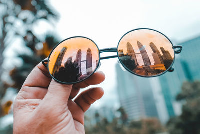 Cropped hand holding sunglasses with reflection of petronas towers