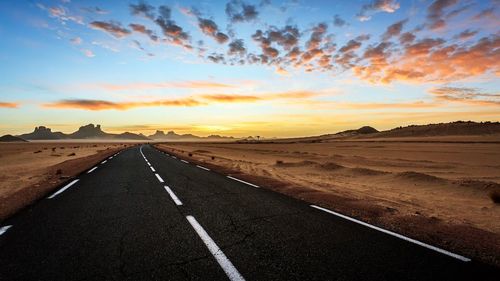 Road by landscape against sky during sunset