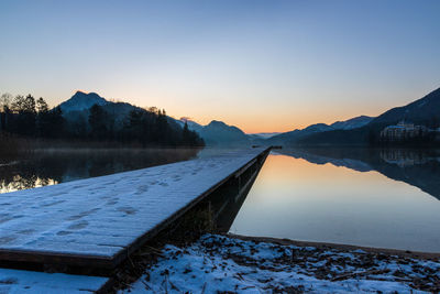 Scenic view of lake by snowcapped mountains against sky during sunset