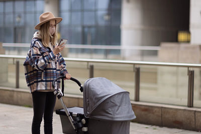 Happy mother walking with stroller in park and using mobile phone. joy of motherhood. stylish woman