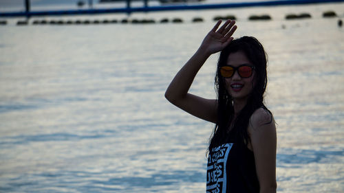 Portrait of young woman waving while standing against sea