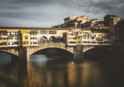 Arch bridge over river by buildings against sky in city