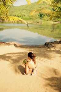 Rear view of woman drinking coconut while sitting by lake