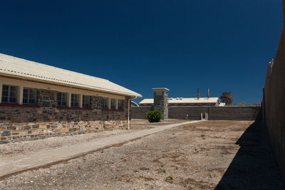 Road by buildings against clear blue sky