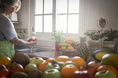 Side view of senior woman cleaning fruits at sink in kitchen