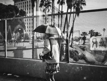 Rear view of woman walking under umbrella on footpath