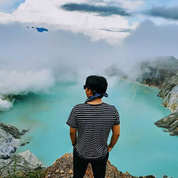 Rear view of man standing on mountain against sky