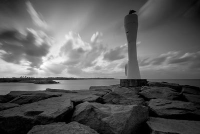 Lighthouse on rock by sea against sky