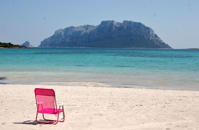 Chair on beach against clear blue sky