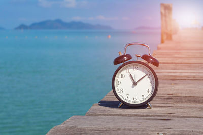 Close-up of clock on table at sea shore against sky