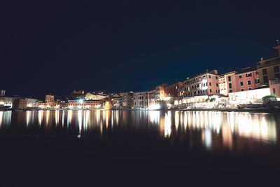 Illuminated buildings by lake against clear sky at night