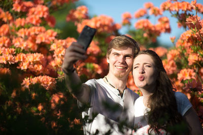 Happy friends taking selfie against flowering plants in park