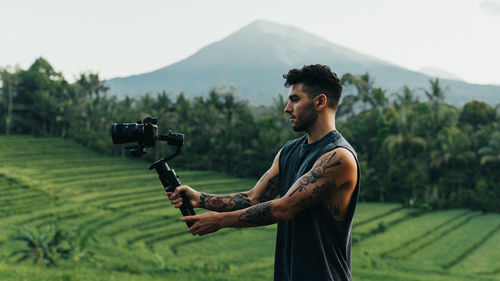 Side view of young man photographing on field