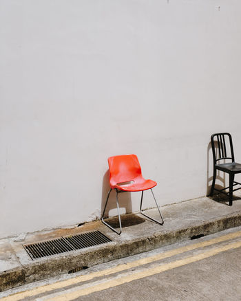 Chairs on sidewalk against white wall on sunny day