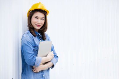 Portrait of a smiling young woman standing against wall