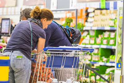 People with shopping cart standing at checkout counter in supermarket