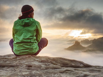 Young active woman with trekking equipment sitting, relaxing and looking at far misty mountains 