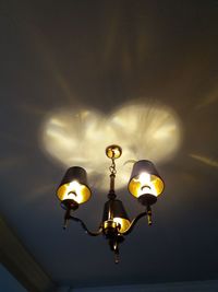 Low angle view of illuminated light bulb hanging against sky