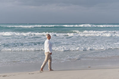Happy caucasian senior woman walking along sandy beach of atlantic ocean, varadero, cuba.
