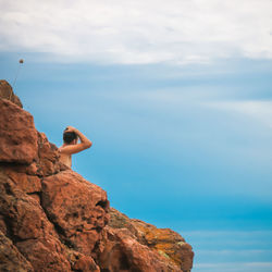 Side view of shirtless man on rock by sea against sky