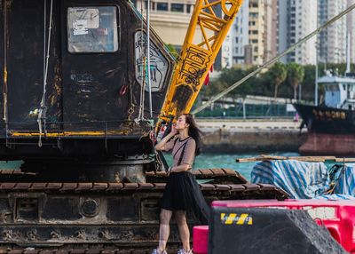 Side view of woman standing by crane at harbor