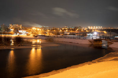 Illuminated buildings by river against sky at night