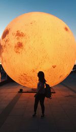 Full length of a girl standing against orange sky