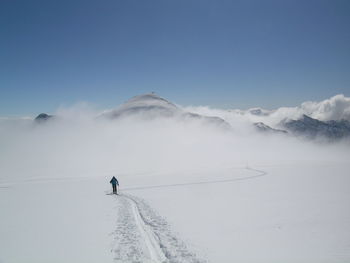 Person skiing on snow covered landscape against clear blue sky