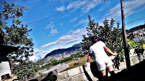 Rear view of people sitting on retaining wall against sky