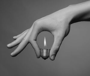 Close-up of hand holding illuminated lighting equipment against gray background