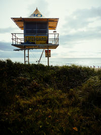 Low angle view of lifeguard hut on field by sea against cloudy sky