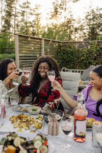 Happy female friends toasting drinks while sitting at dining table during dinner party