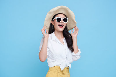 Young woman wearing sunglasses standing against blue sky