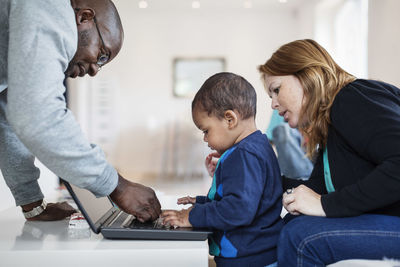 Side view of parents assisting son in using laptop at home