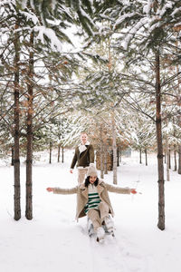 A man and a woman in love have fun and ride a sleigh in the forest among the trees in winter 