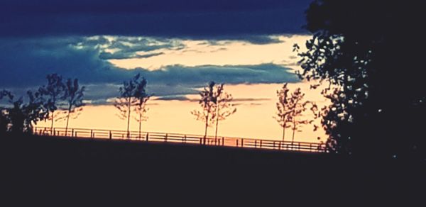 Silhouette trees on landscape against sky at sunset