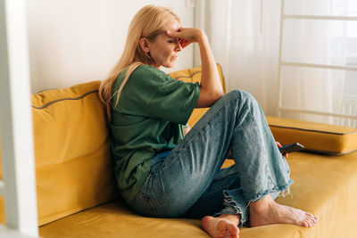 Depressed sad middle aged woman sitting on sofa at home. person