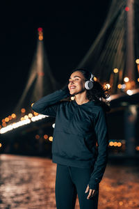 Young woman standing against illuminated city at night