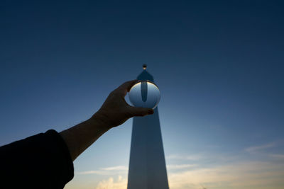 Low angle view of hand holding lighthouse against sky during sunset