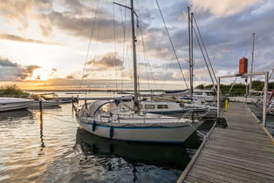 Sailboats moored in sea against sky during sunset