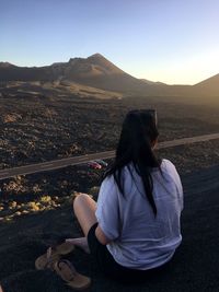 Woman sitting on mountain against clear sky