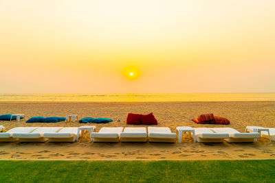 Lounge chairs on beach against sky during sunset