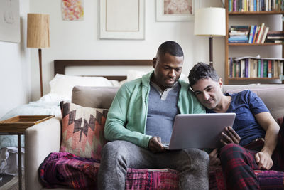 Multi-ethnic homosexual males using laptop on sofa at home