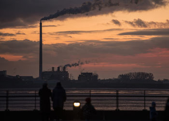 Silhouette people standing by river against sky during sunset