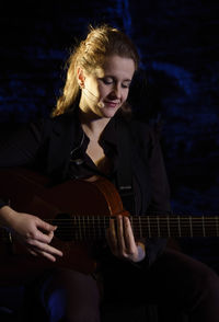 Woman playing guitar while sitting on stage