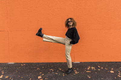 Side view of woman standing against orange wall