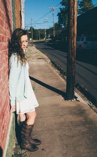 Side view of young woman standing against brick wall in city