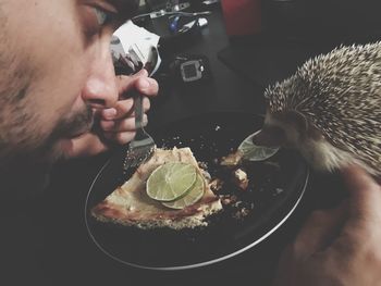 Close-up of man eating food while looking at hedgehog